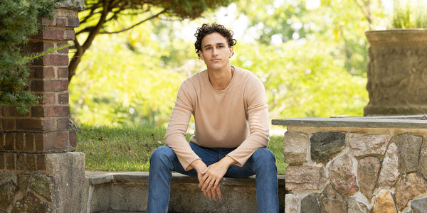 male model sitting on rock steps wearing nomad crewneck in camel