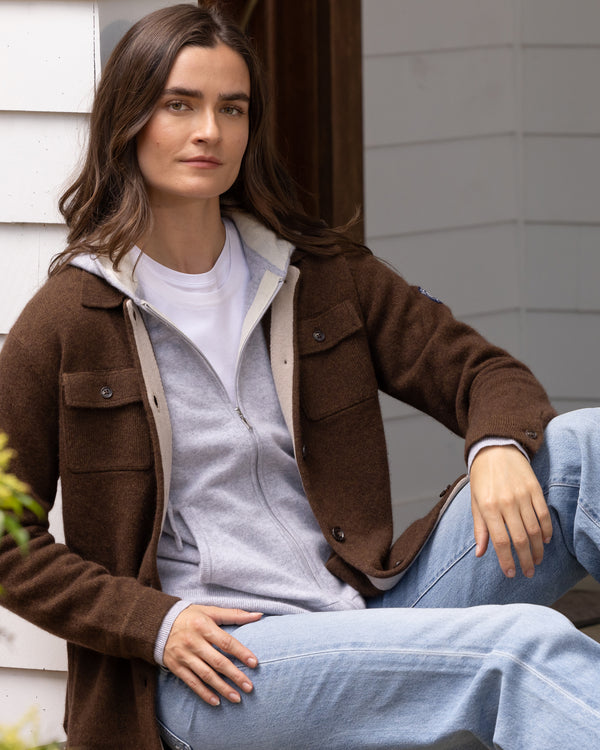 Woman sitting outside wearing cashmere shirt jacket in mocha and underneath the Madison Zip Hoodie in Sterling